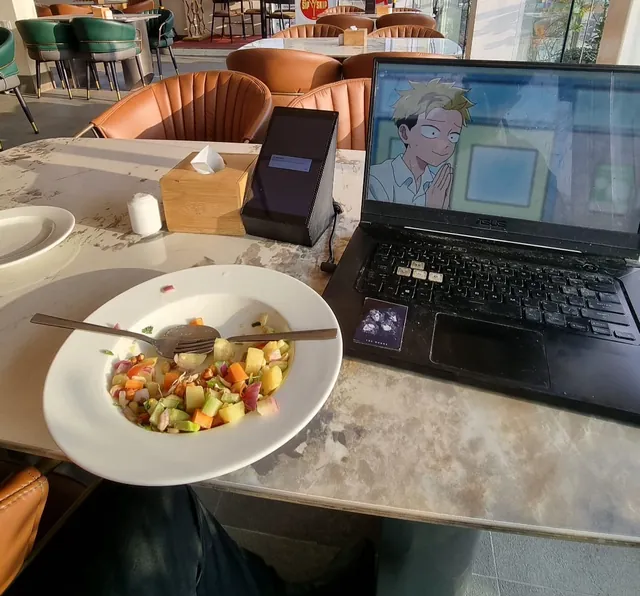 A fruit salad next to a laptop playing anime at a rooftop café